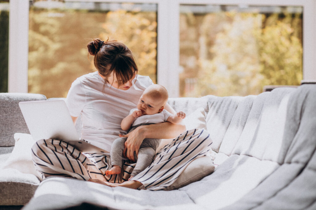 Moeder met baby op de bank achter een laptop tijdens het opstellen van een postpartum plan
